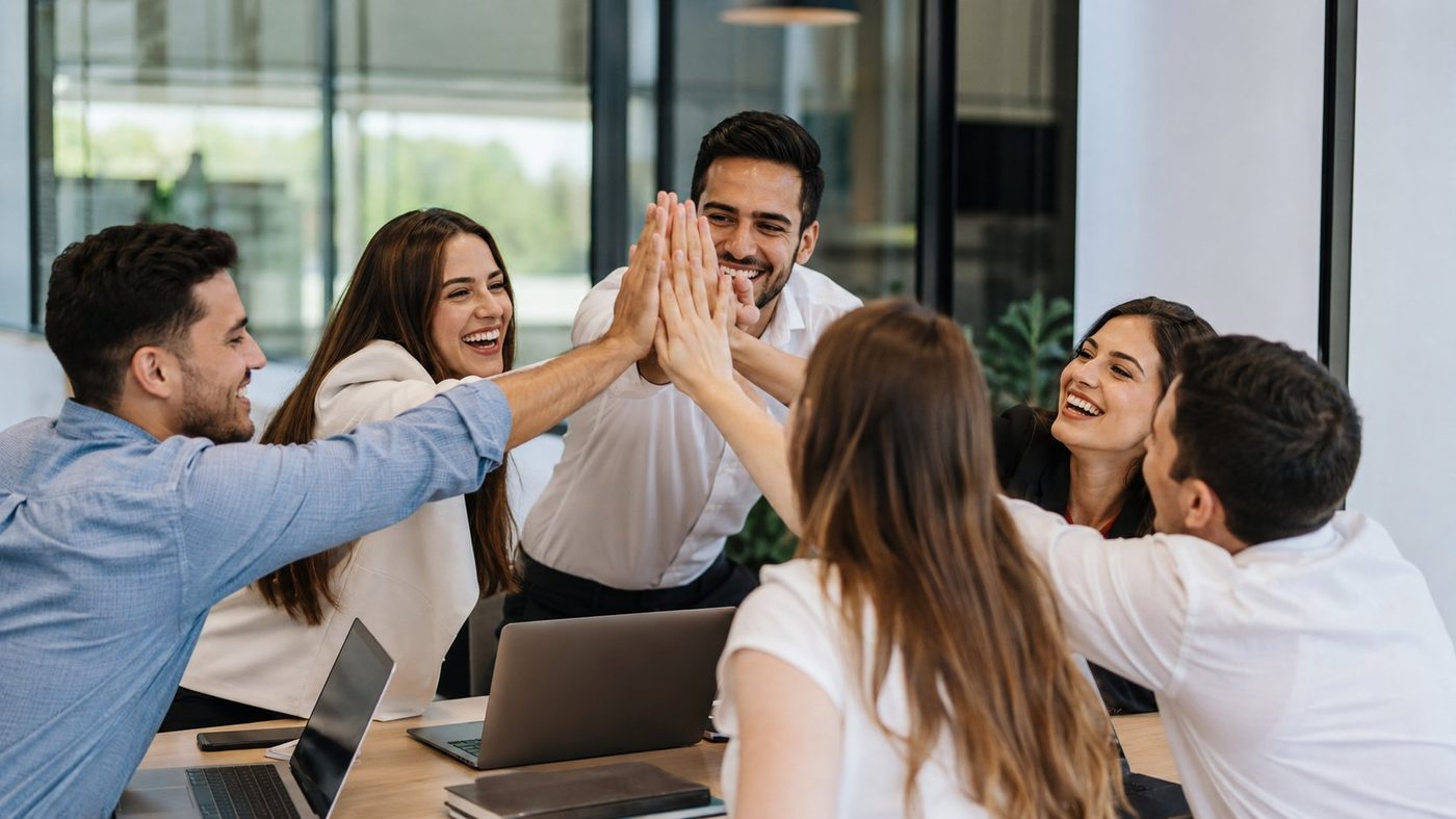 Equipo joven celebrando con un choque de manos en una sala de reuniones